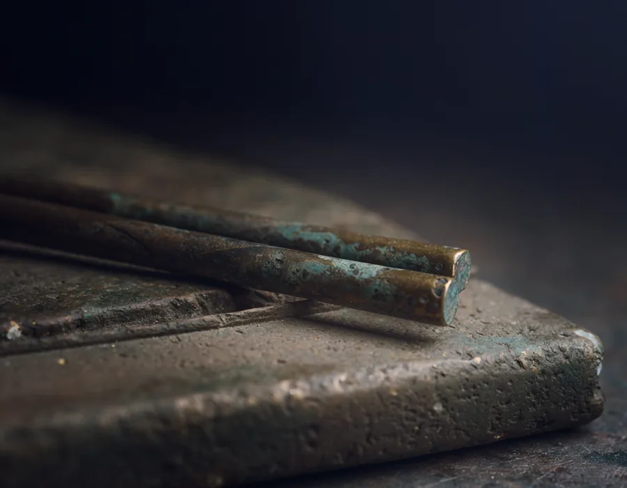 Ancient bronze chopsticks resting on a weathered stone slab.