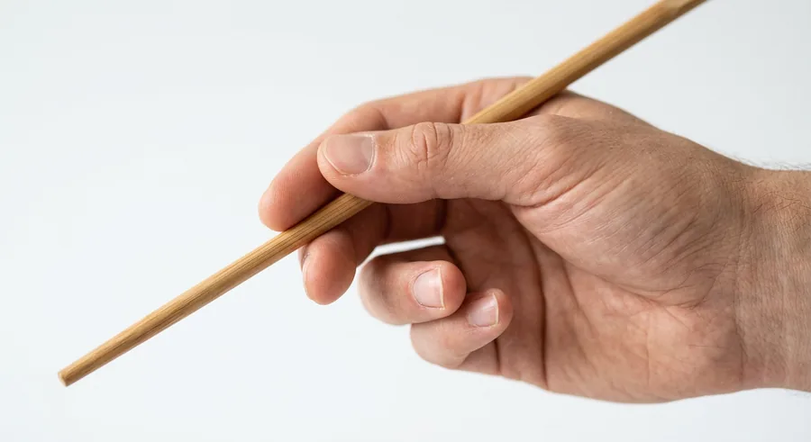 A single chopstick resting in the crook of a hand between the thumb and index finger.