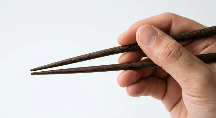 A close-up of chopsticks in motion, showing the top chopstick moving while the bottom stays still.